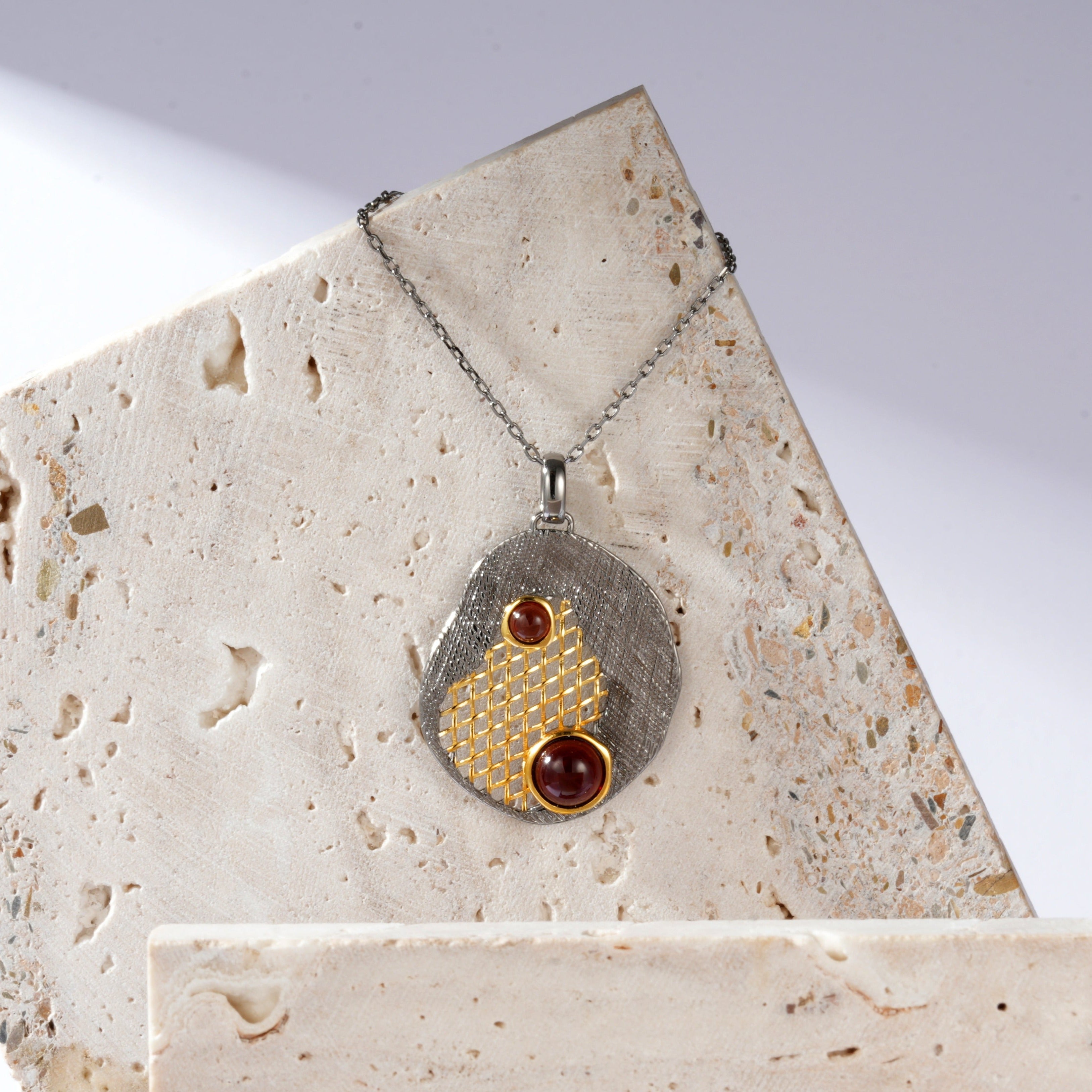 A silver gold plated necklace with red garnet stones and black rhodium.