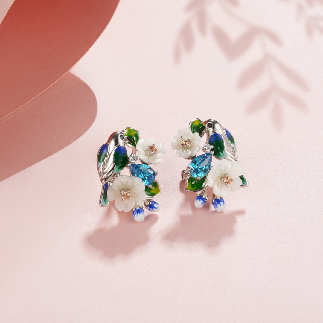 A pair of silver earrings with blue stones, enamel, shell flowers and a bird charm.