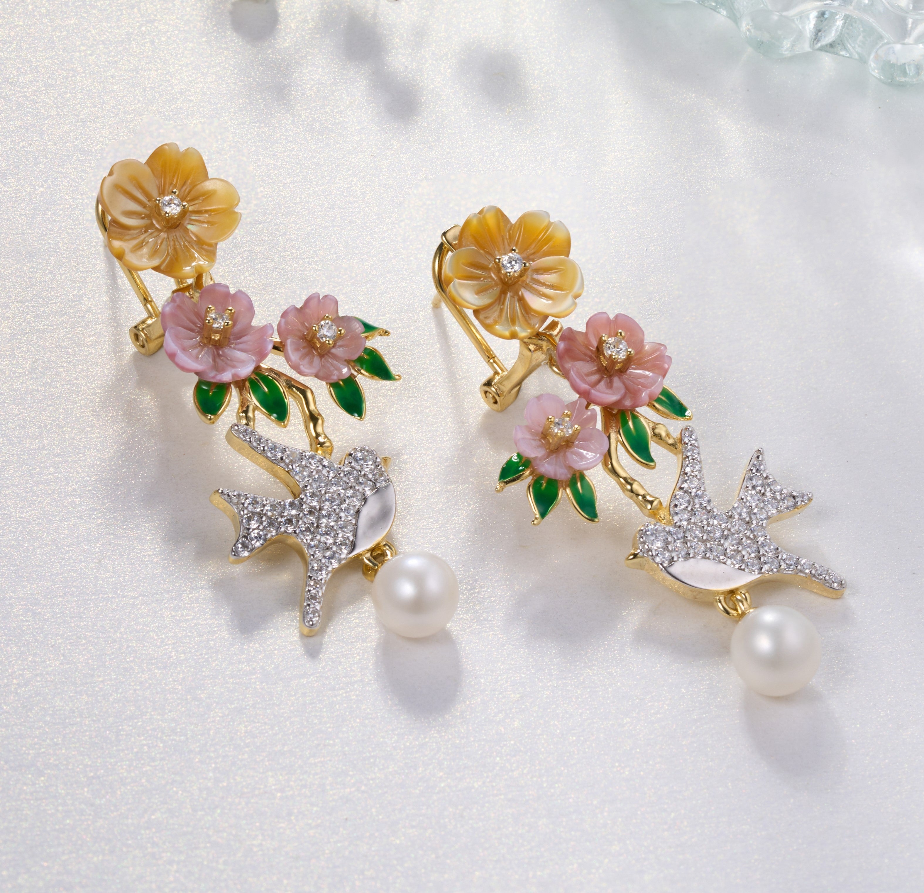 A pair of gold plated earrings with pearls, green stones, yellow, purple, pink shell flowers and a bird charm.