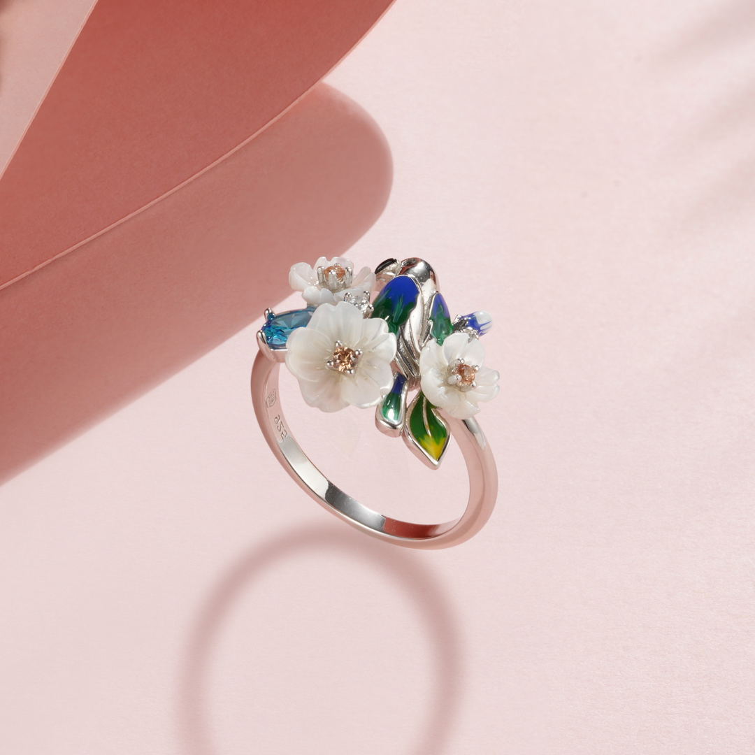 A silver ring with enamel, shell flowers, blue stones and a bird charm.
