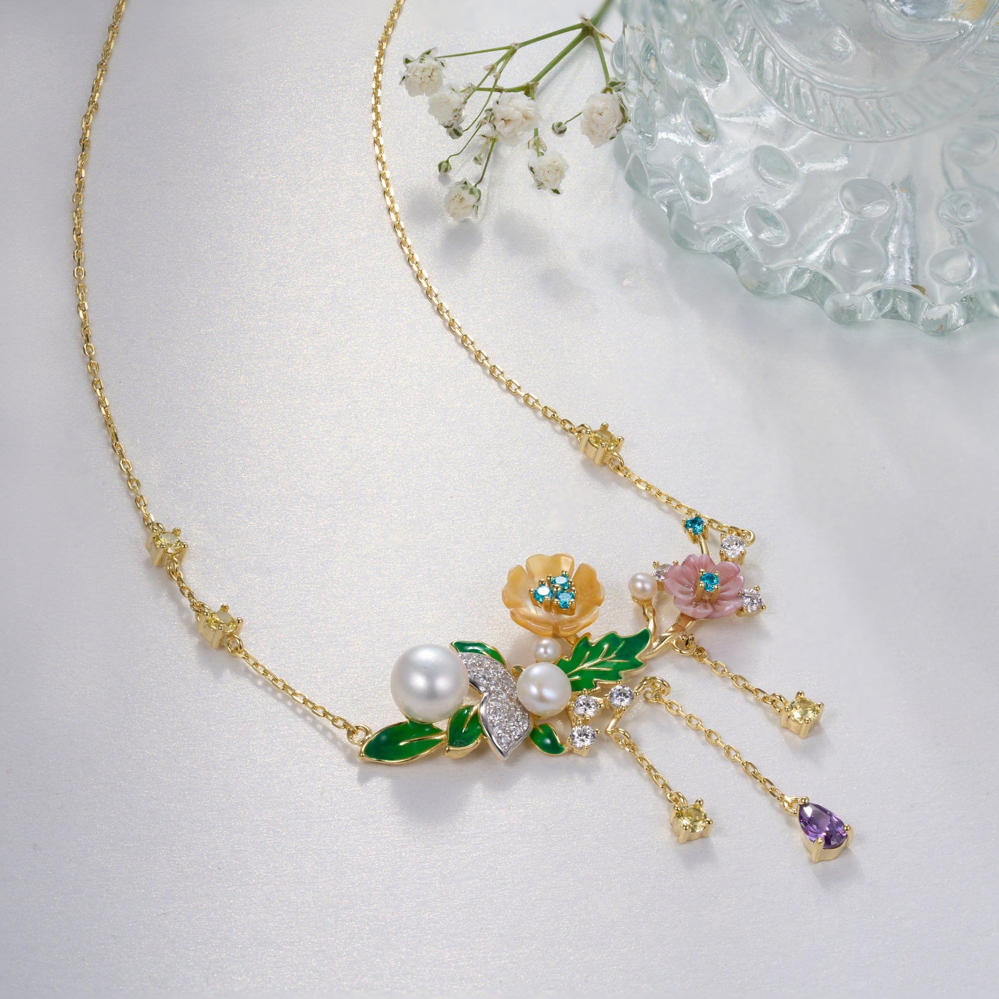 A gold plated necklace with pearls, green stones, yellow, purple, pink shell flowers and a bird charm.